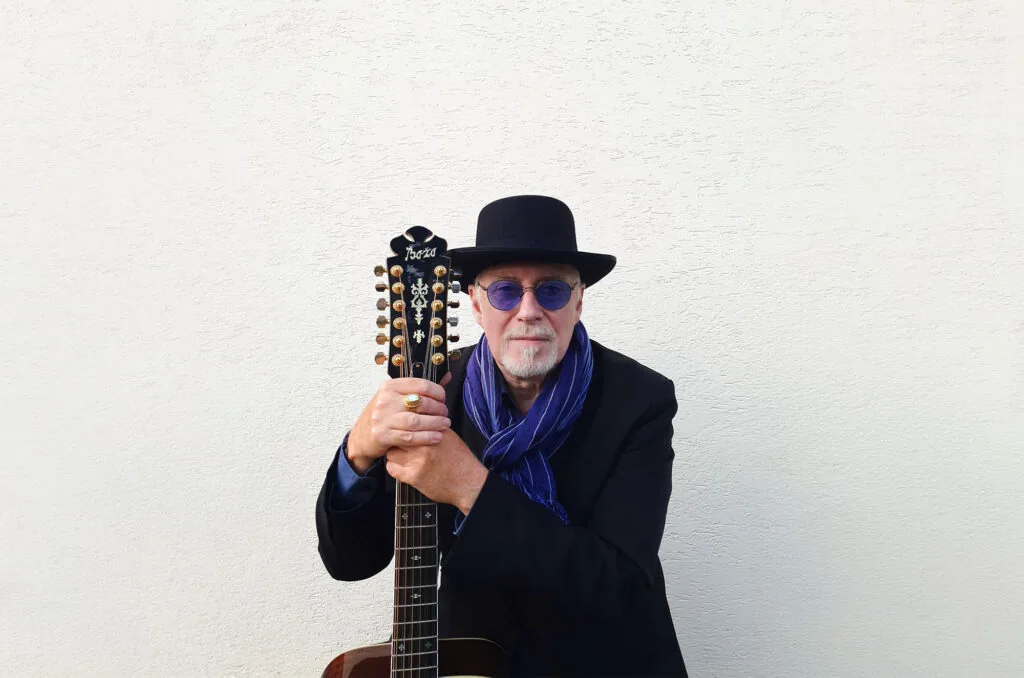 Michael Phillips mit Hut, blauer Brille und seiner zw&ouml;lfsaitigen Gitarre